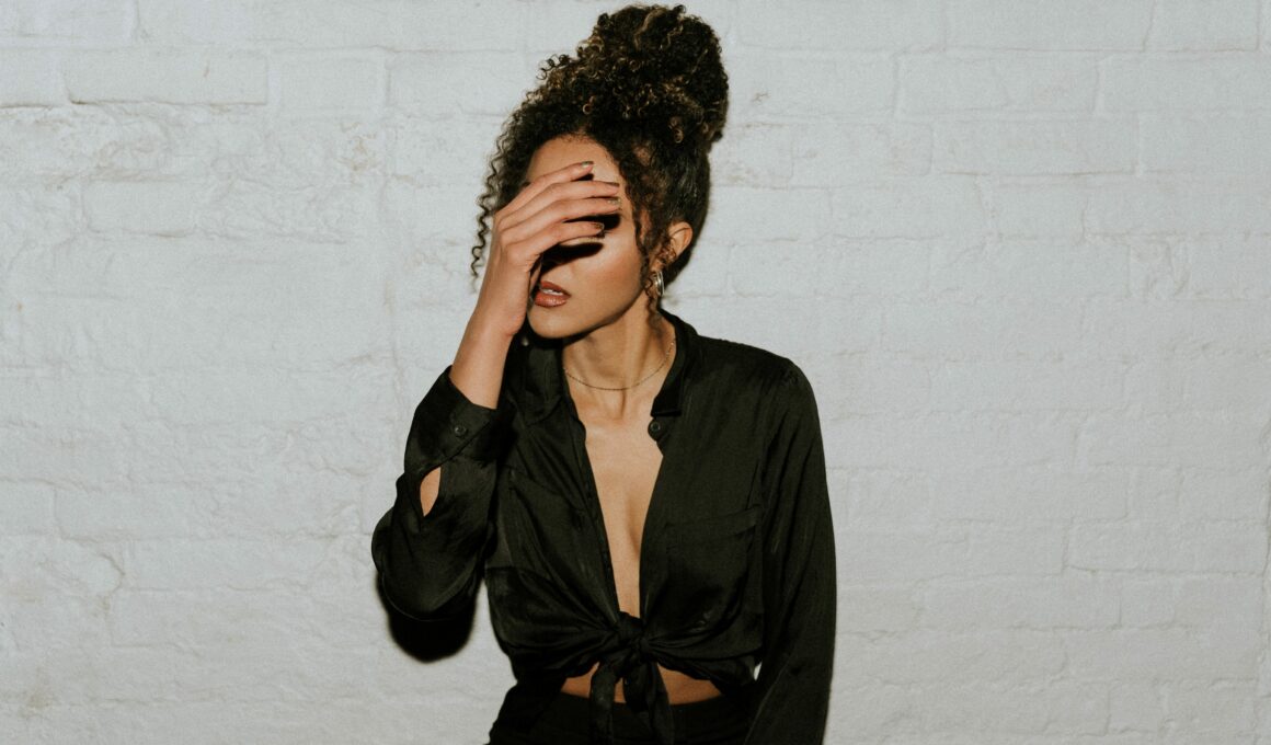 A woman covers her face against a off white grey brick wall lit by strong lighting