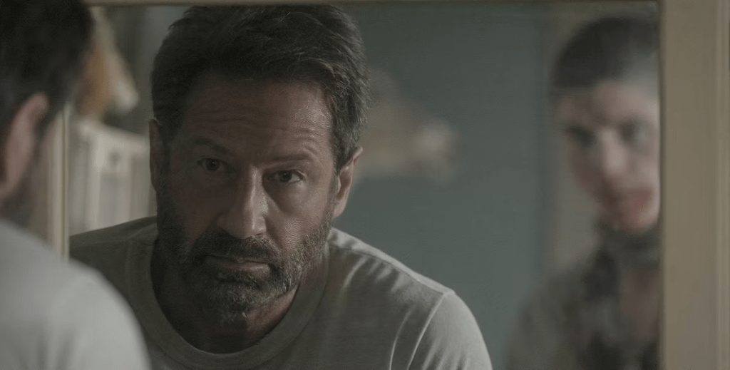 Actor David Duchovny stares into the mirror as a ghostly looking person stands in the background.