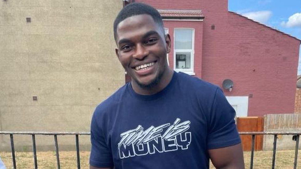 Chris Kaba smiles wearing a blue t-shirt.