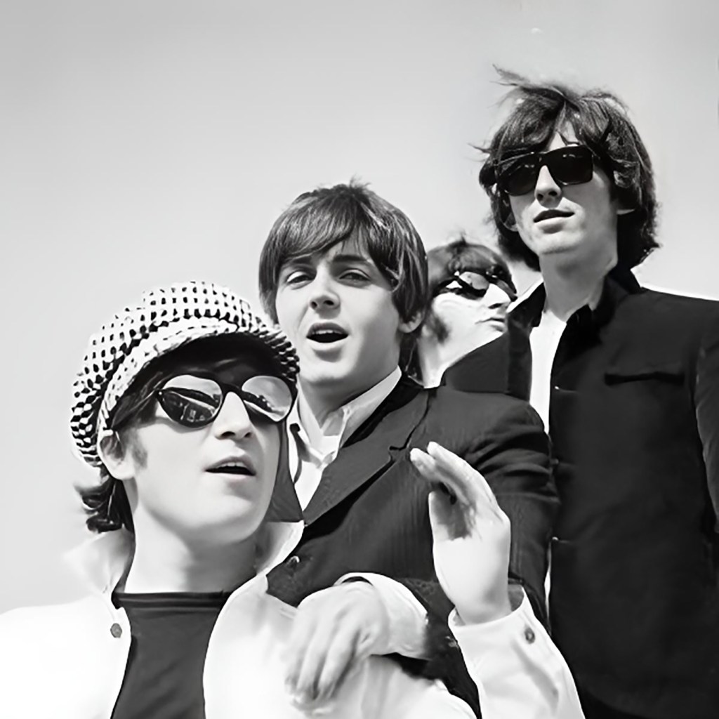 The Beatles appear to be standing on the steps of a plane laughing and enjoying themselves wearing sunglasses, hats and singing.