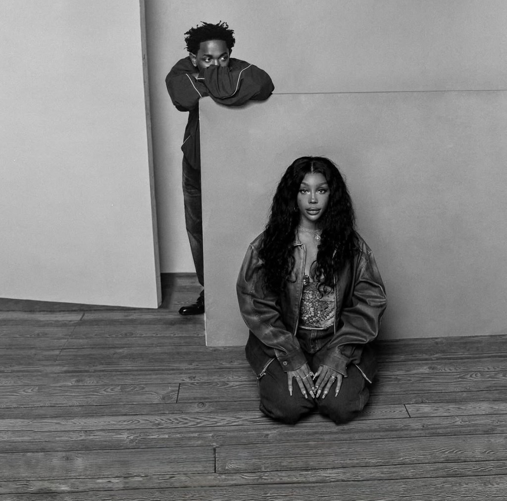 Kendrick Lamar leans forward against a wooden backdrop, gazing to his left, while SZA kneels in the foreground, her hands resting on her knees.