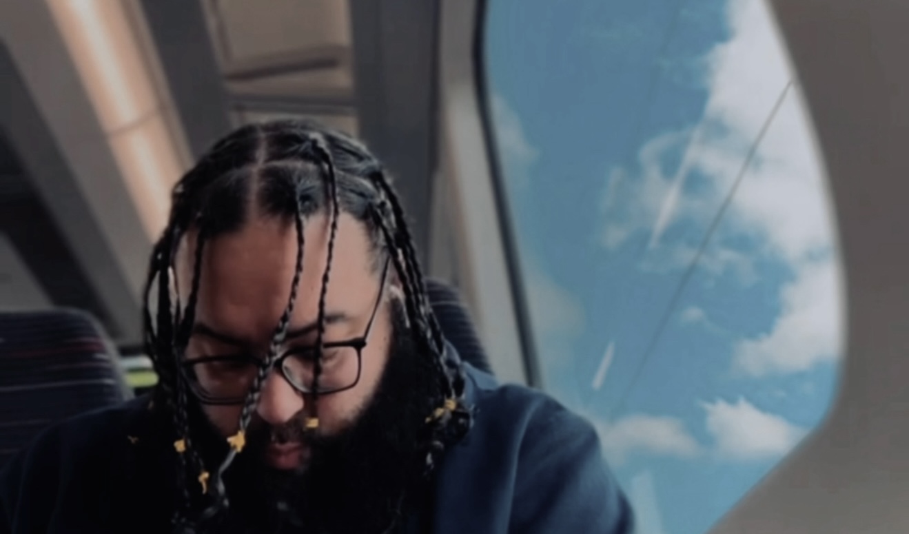 UK rapper Scrulove sitting by a window on a train, contemplating for press still of new single 'Glory' from his 2025 album.