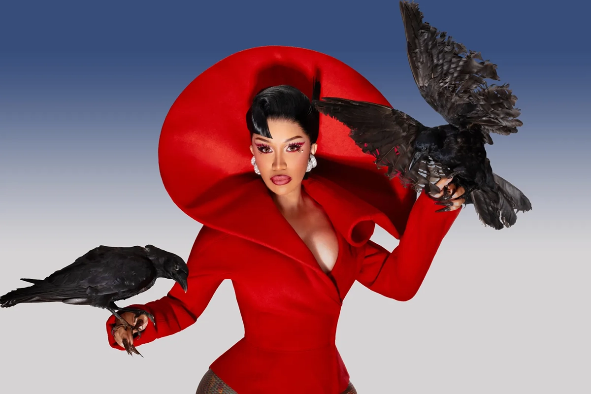 Cardi B holds a crow in each hand while wearing a red high-fashion outfit.