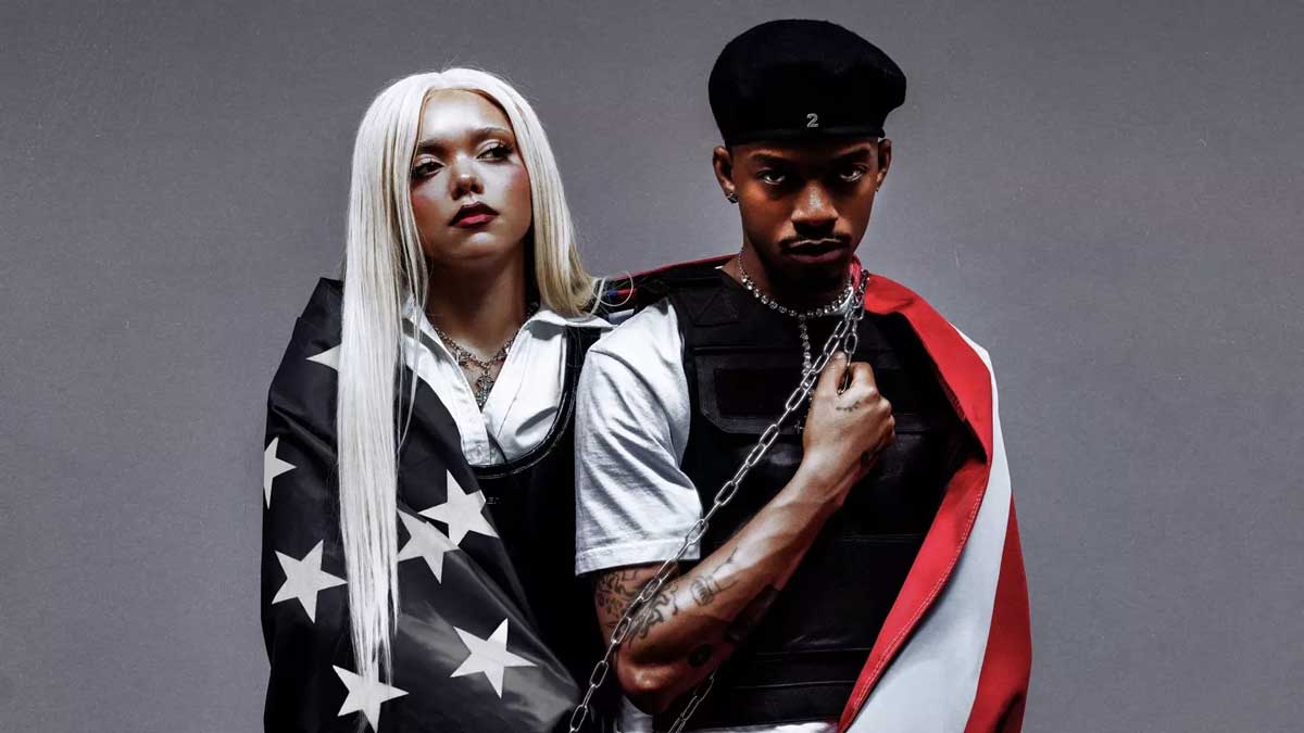 SWIM and Jadagrace of PARTYOF2 standing draped in the American flag against a grey backdrop.