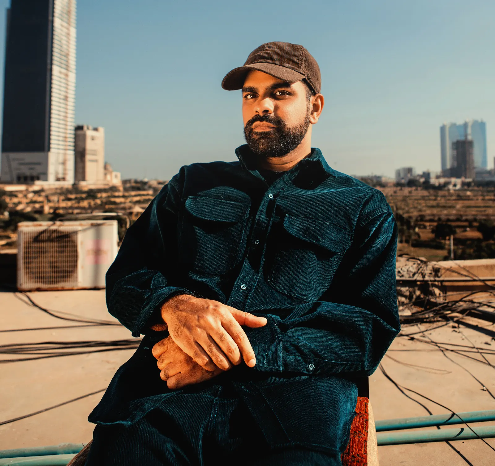 Ahadadream seated on a rooftop chair at golden hour, wearing a baseball cap.