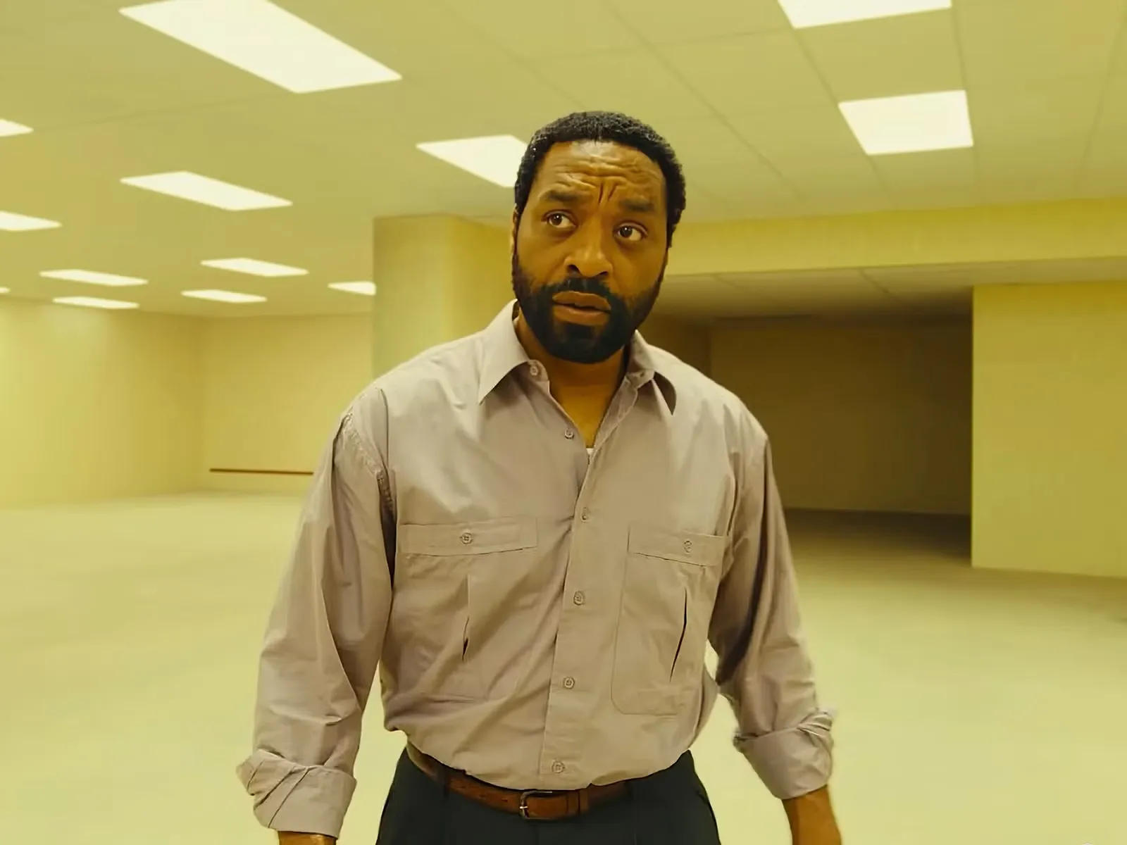 Chiwetel Ejiofor as Clark probes the Backrooms for the first time, wearing a shirt and suit trousers as he carefully navigates the maze-like, fluorescent-lit corridors.