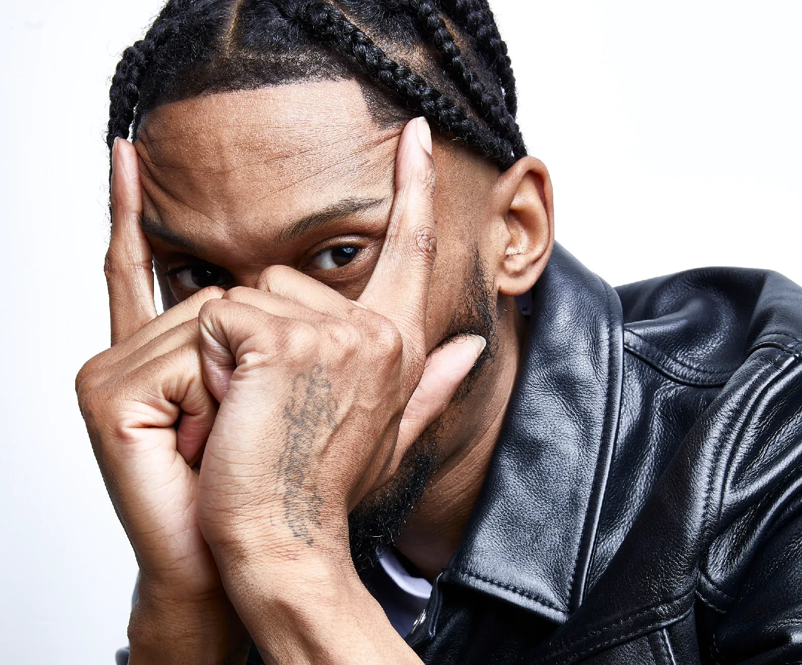 Scorcher, wearing a black leather jacket, poses for a press still for his new album, 'ADMD', against a white background.
