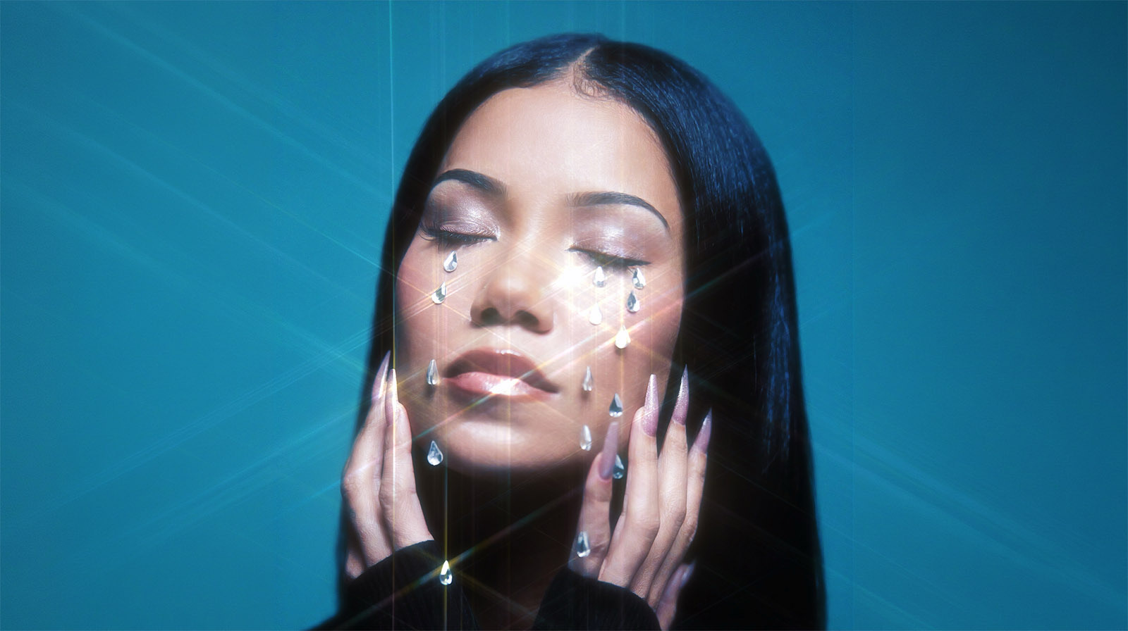 Jhené Aiko with her eyes closed, posing against a blue background with crystal teardrops on her face and a soft starburst light effect.