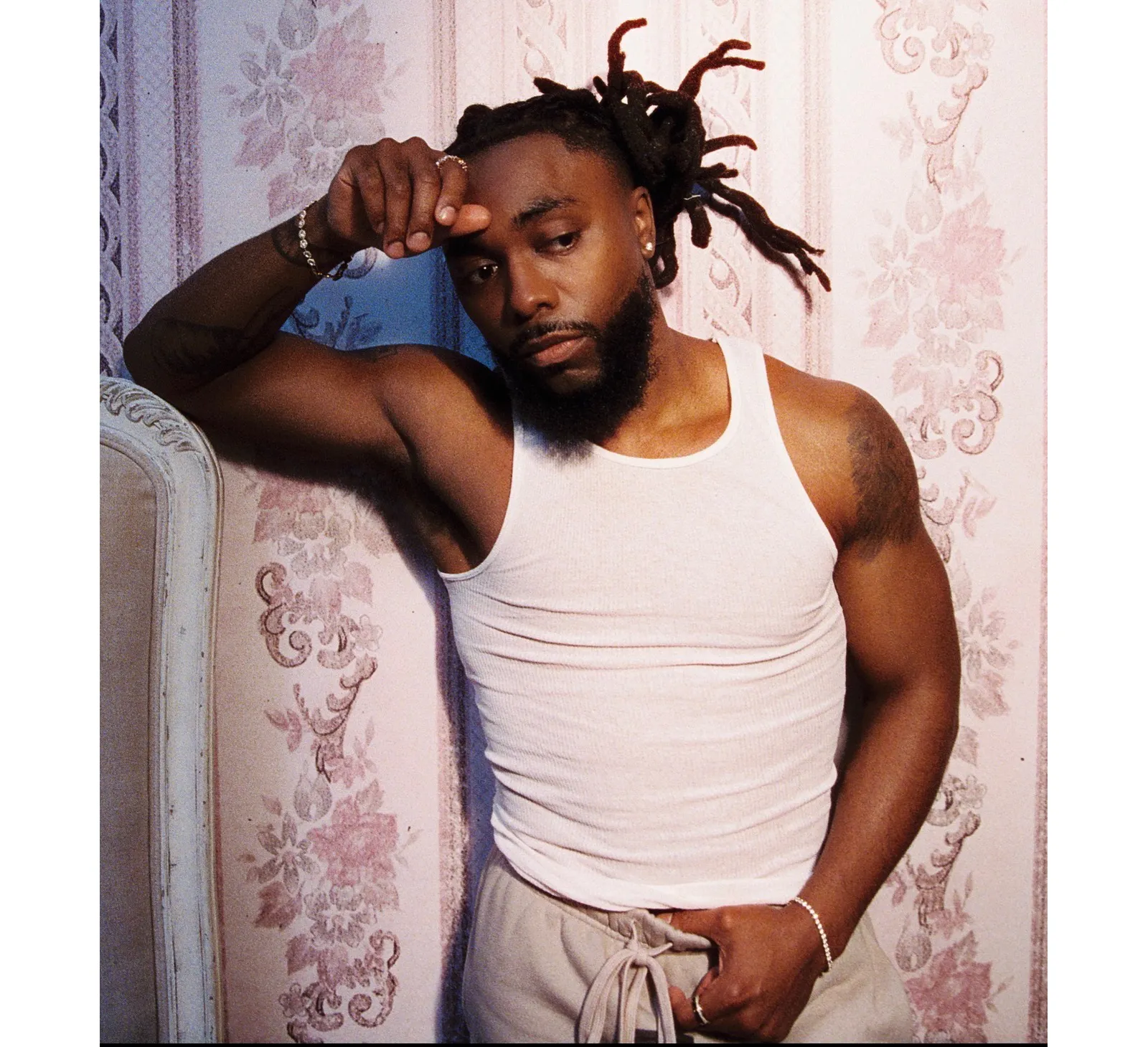 Johnny Venus poses in a white vest against floral wallpaper for his new R&B single “Sarahtonin”.