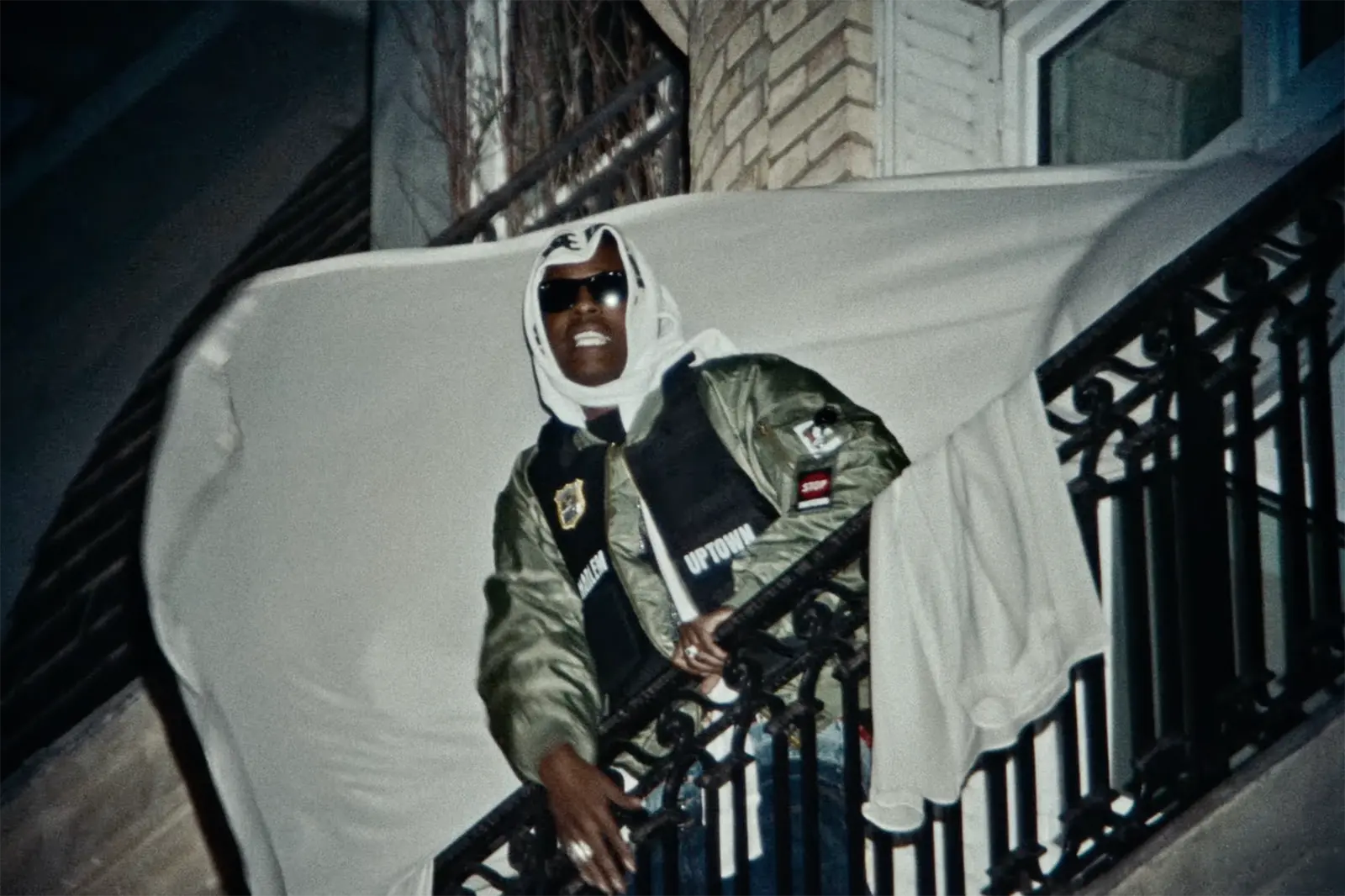 A$AP Rocky stands on a balcony at night as white sheets billow around him in the music video for “SWAT TEAM”.