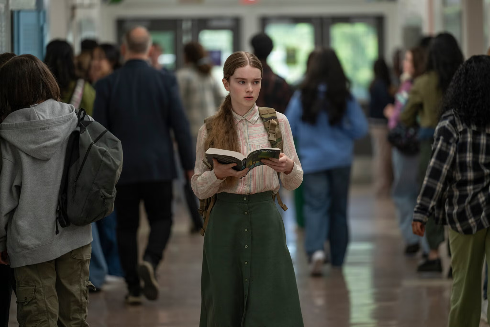 Summer H. Howell as Carrie White, holding an open book while walking through a crowded school corridor in the 2026 television adaptation of Stephen King's Carrie.