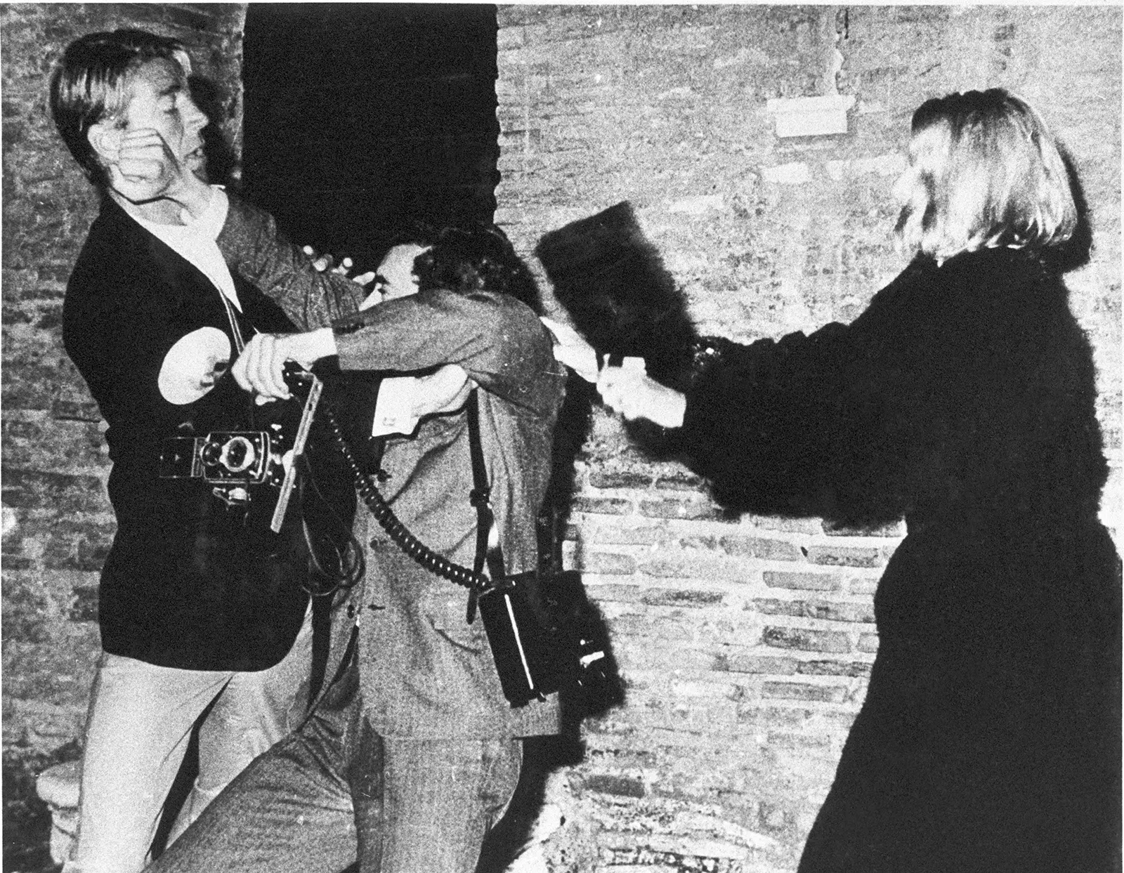 Black-and-white photograph of Mickey Hargitay confronting paparazzi photographer Rino Barillari as Vatussa Vitta strikes him with her handbag on Via Veneto in Rome, 1963.